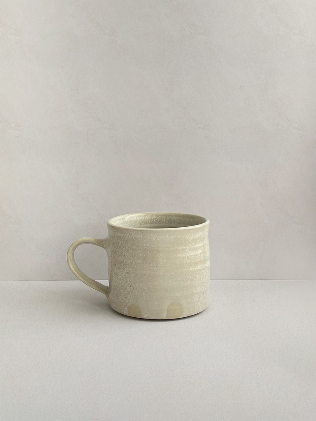 A beige handmade ceramic espresso mug with a handle, on a neutral background - right side view.