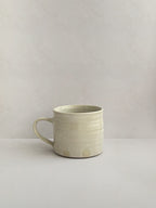 A beige handmade ceramic espresso mug with a handle, on a neutral background - right side view.