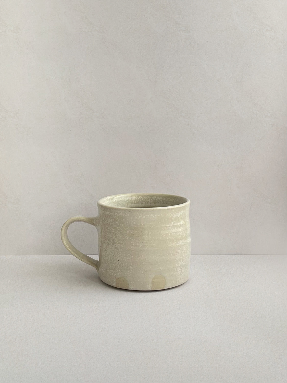 A beige handmade ceramic espresso mug with a handle, on a neutral background - right side view.
