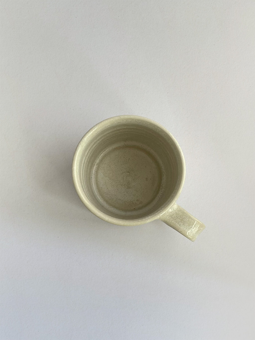 A beige handmade ceramic espresso mug with a handle, on a neutral background - top view.
