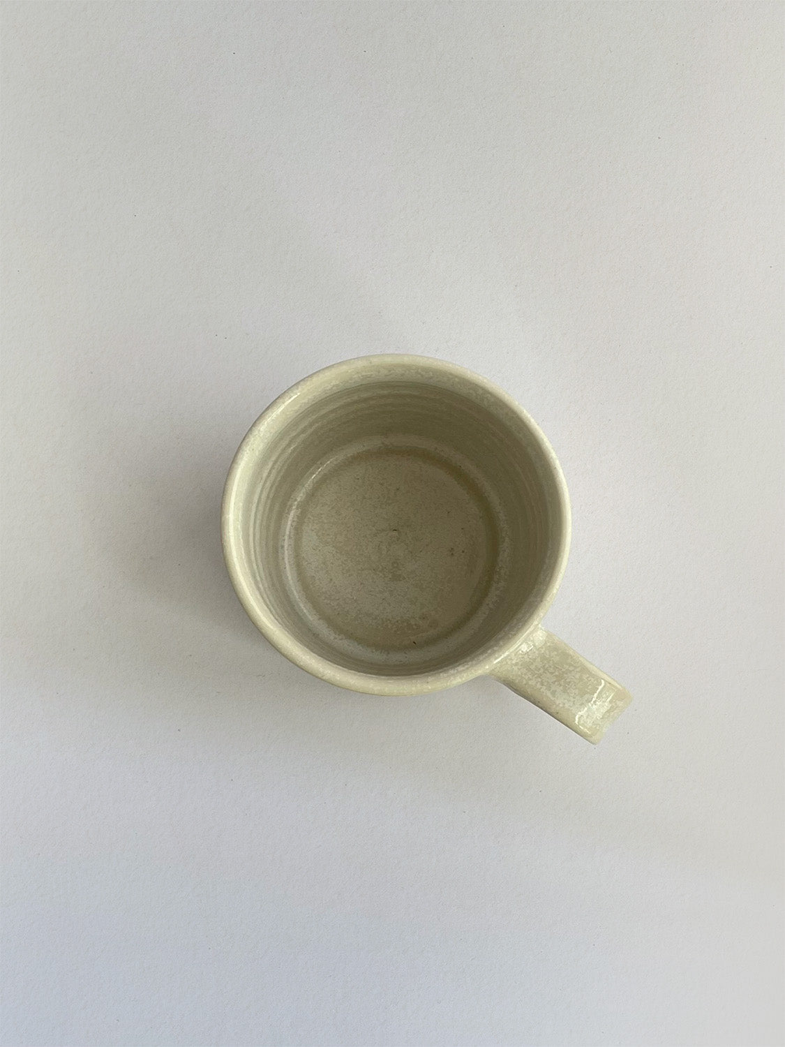 A beige handmade ceramic espresso mug with a handle, on a neutral background - top view.
