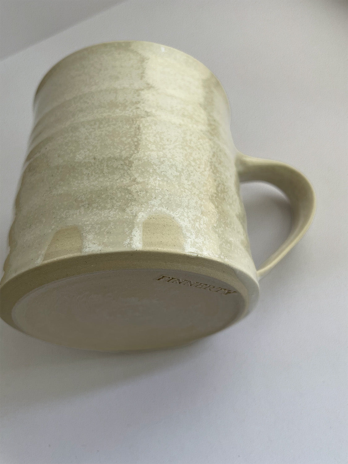 A hand-thrown ceramic mug with a handle, in a beige speckled glaze on a neutral background - detail view.