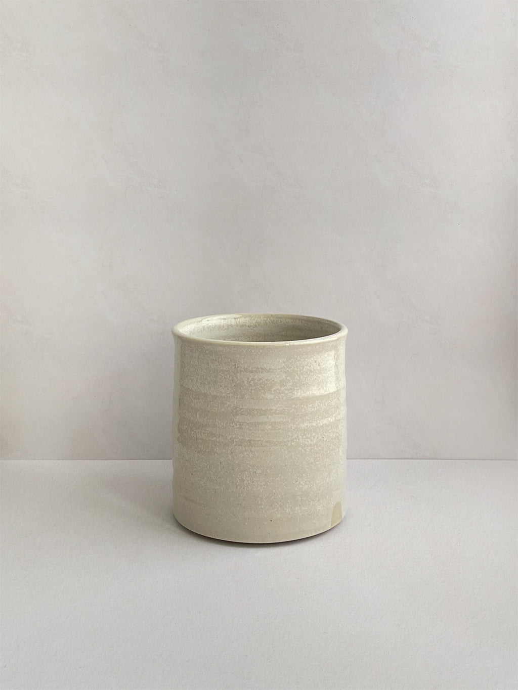 A hand-thrown ceramic mug with a handle, in a beige speckled glaze on a neutral background - front view.