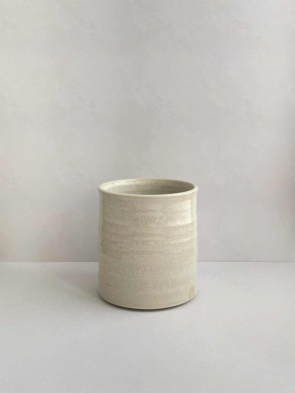 A hand-thrown ceramic mug with a handle, in a beige speckled glaze on a neutral background - front view.