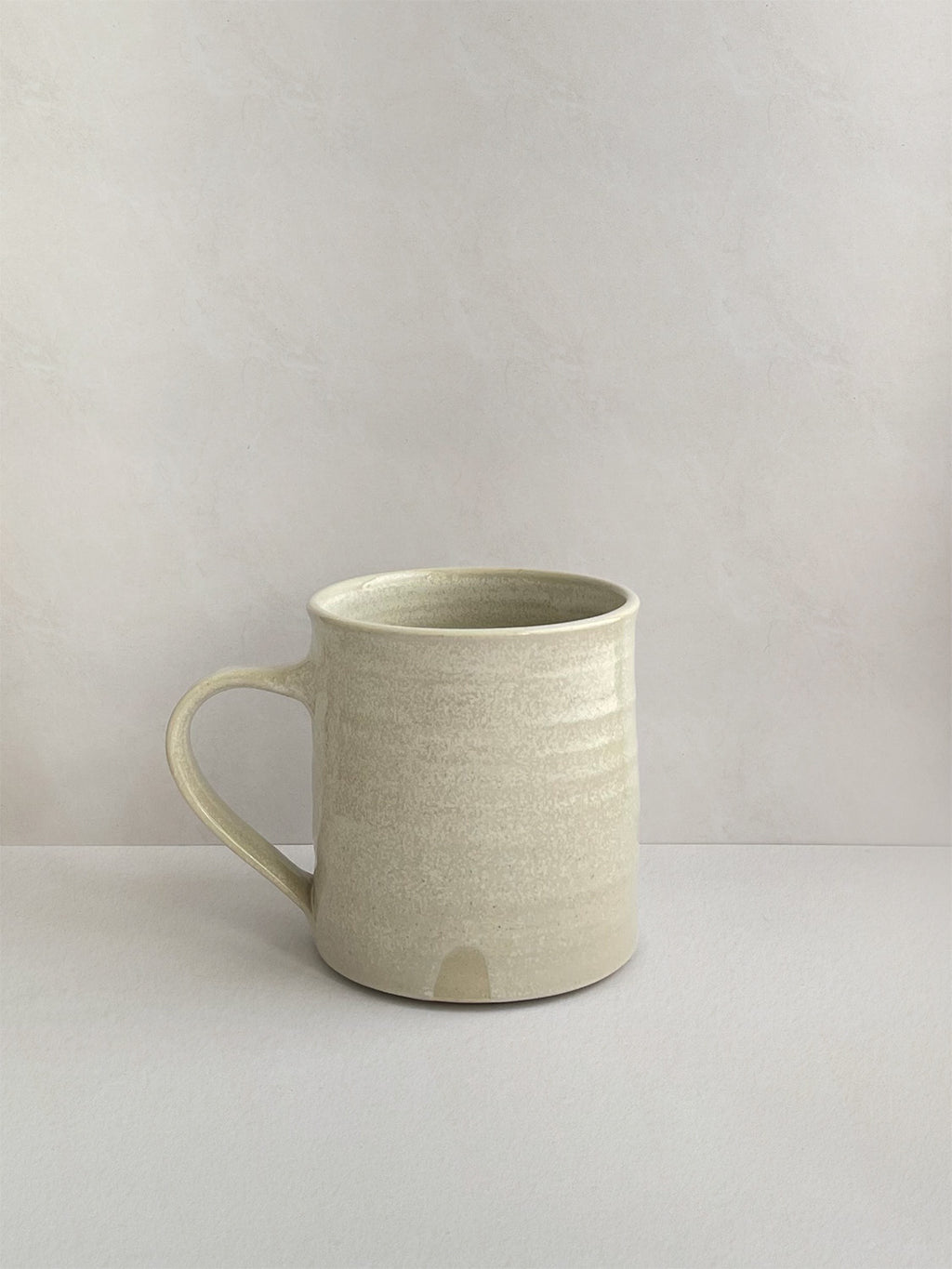 A hand-thrown ceramic mug with a handle, in a beige speckled glaze on a neutral background - right side view.