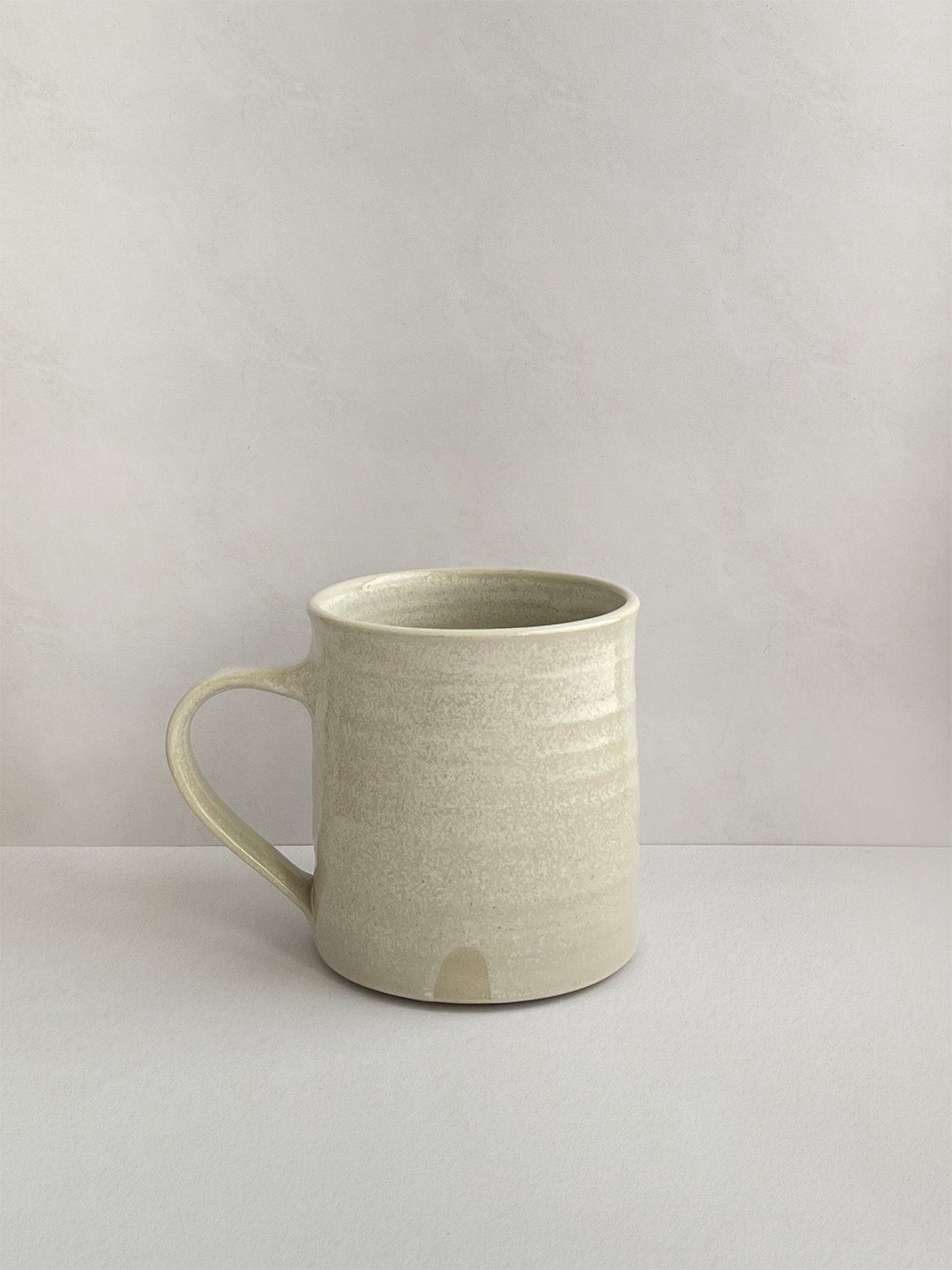 A hand-thrown ceramic mug with a handle, in a beige speckled glaze on a neutral background - right side view.