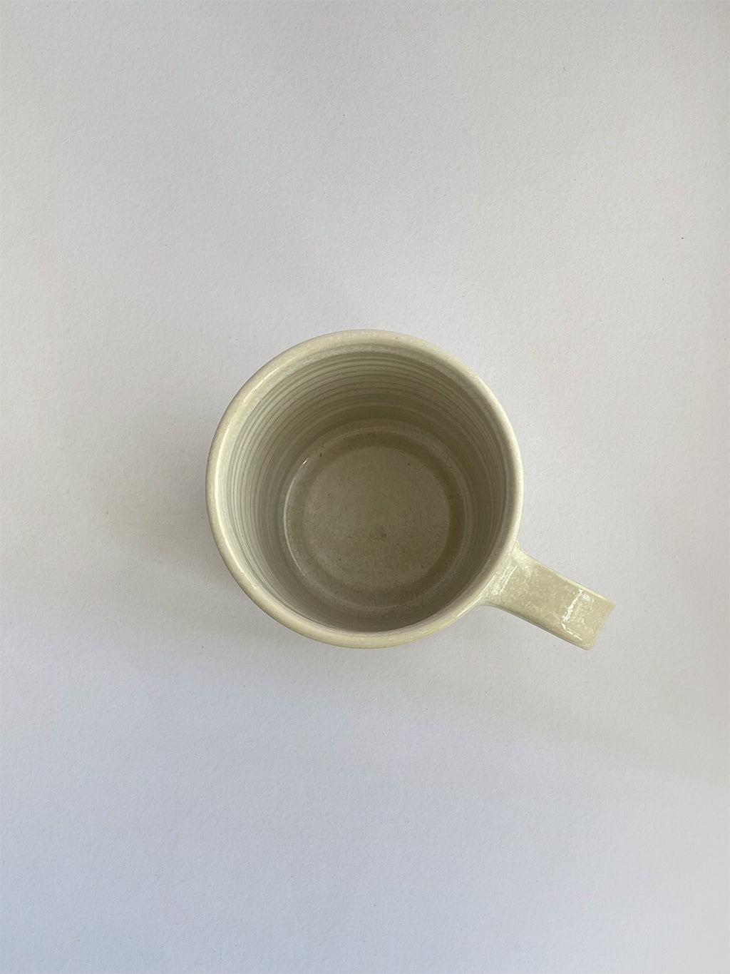 A hand-thrown ceramic mug with a handle, in a beige speckled glaze on a neutral background - top view.