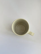 A hand-thrown ceramic mug with a handle, in a beige speckled glaze on a neutral background - top view.