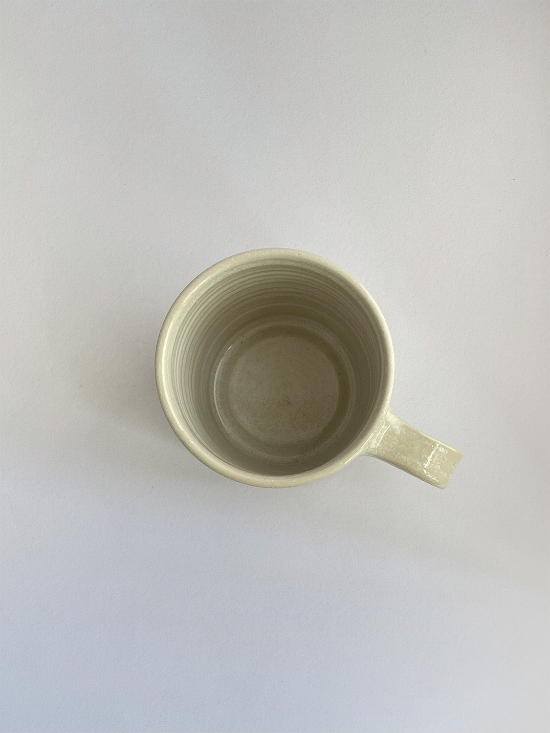 A hand-thrown ceramic mug with a handle, in a beige speckled glaze on a neutral background - top view.
