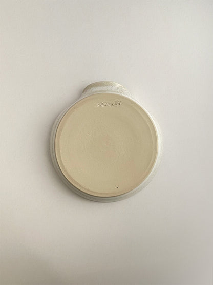 Warm white mottled ceramic spoon rest on a neutral background - base view.