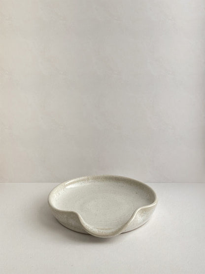 Warm white mottled ceramic spoon rest on a neutral background - front view.
