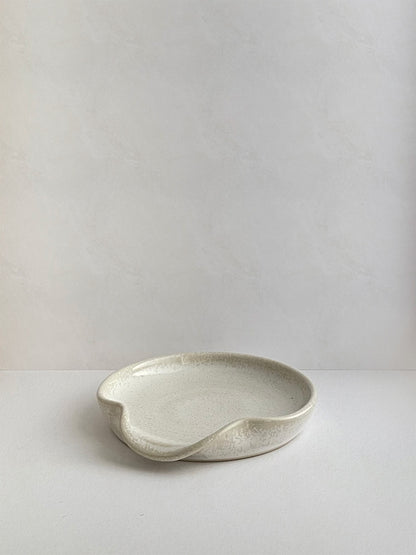Warm white mottled ceramic spoon rest on a neutral background - front view.