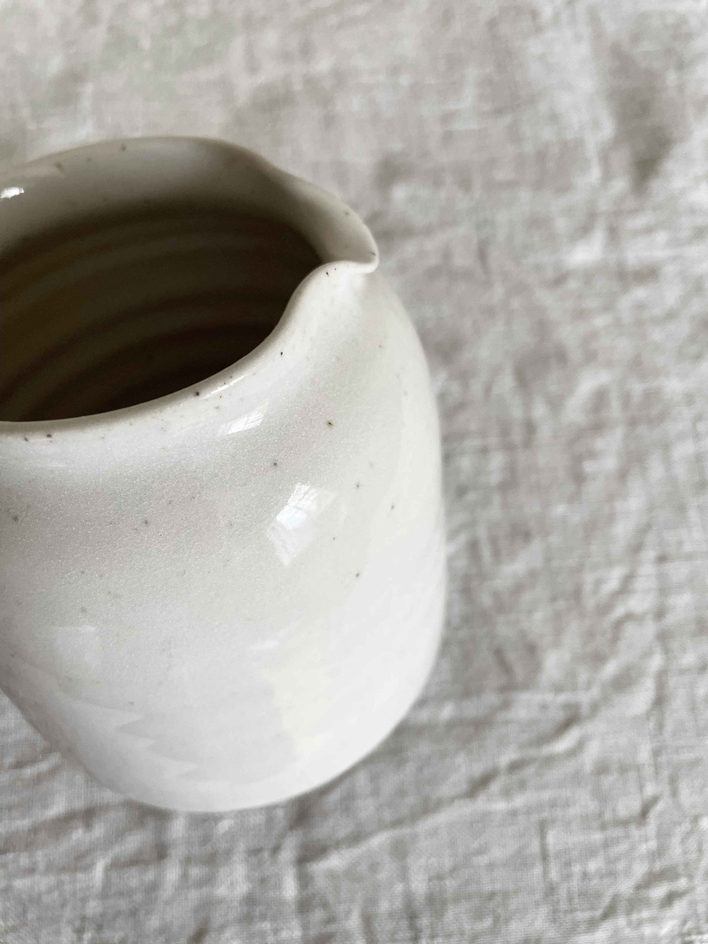 Ceramic jug with handle in glossy white speckled glaze - close-up.