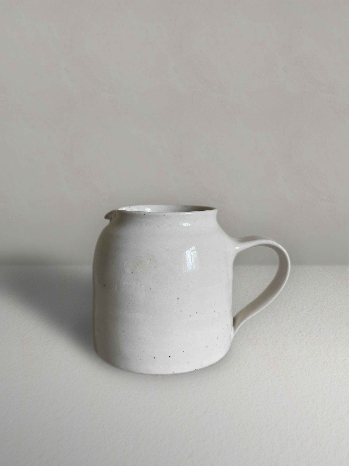 Ceramic jug with handle in glossy white speckled glaze - front.