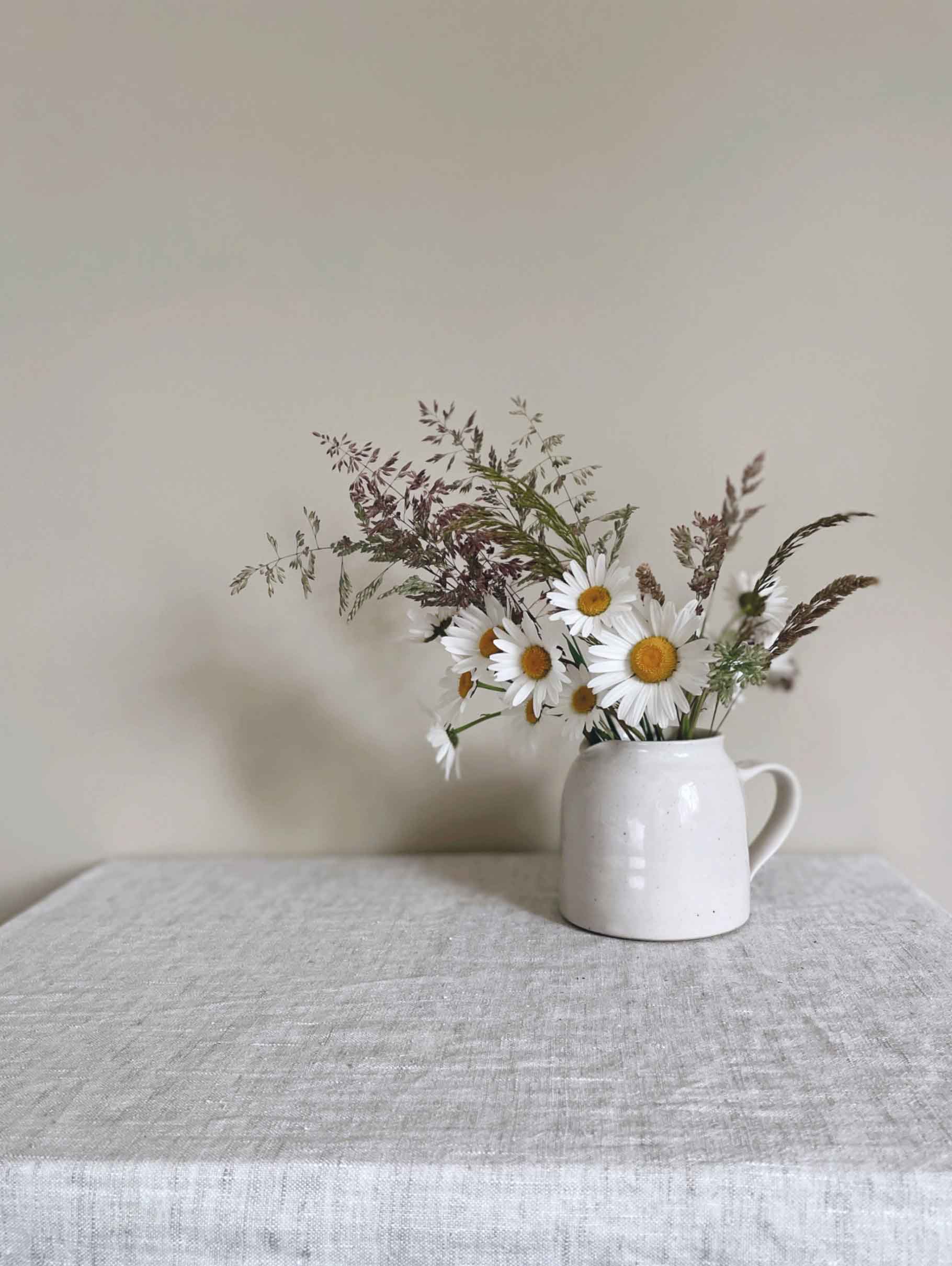 Ceramic jug with handle in glossy white speckled glaze with small bunch of wildflowers.