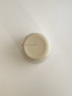 Speckled white ceramic cup on a neutral background - base view.