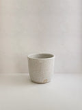 Speckled white ceramic cup on a neutral background - front view.