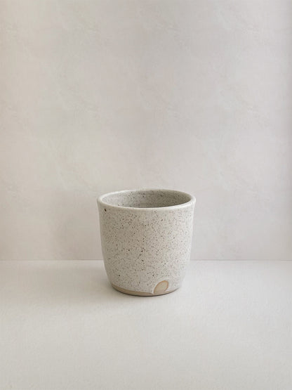 Speckled white ceramic cup on a neutral background - front view.