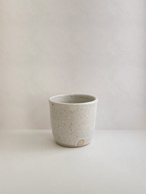 Speckled white ceramic cup on a neutral background - front view.