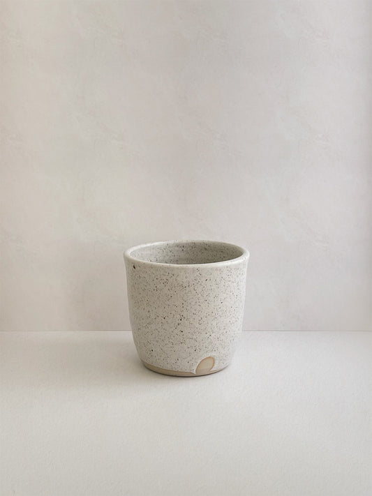 Speckled white ceramic cup on a neutral background - front view.