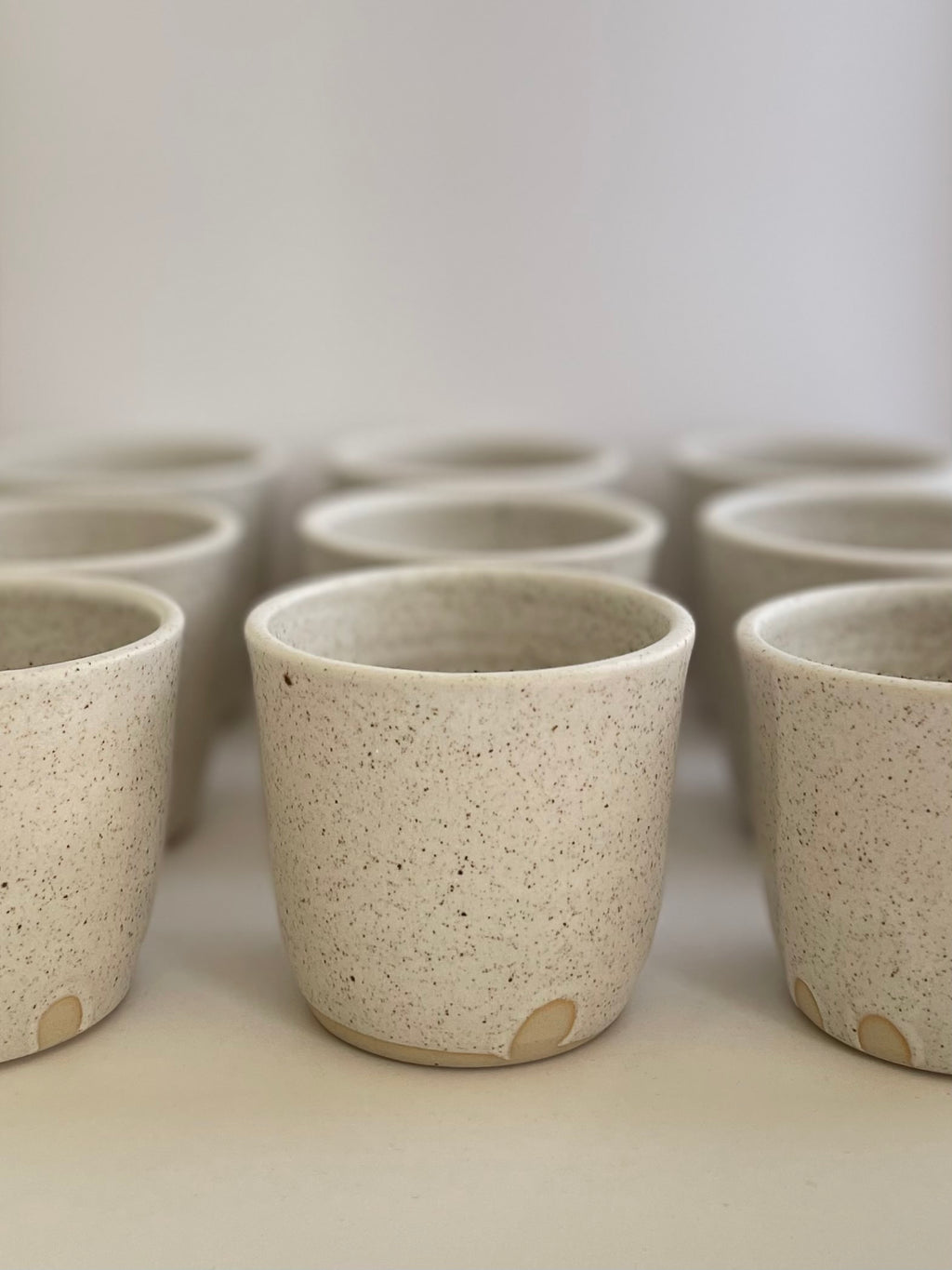 Collection of handmade ceramic coffee cups in a soft white speckled glaze.