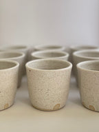Collection of handmade ceramic coffee cups in a soft white speckled glaze.