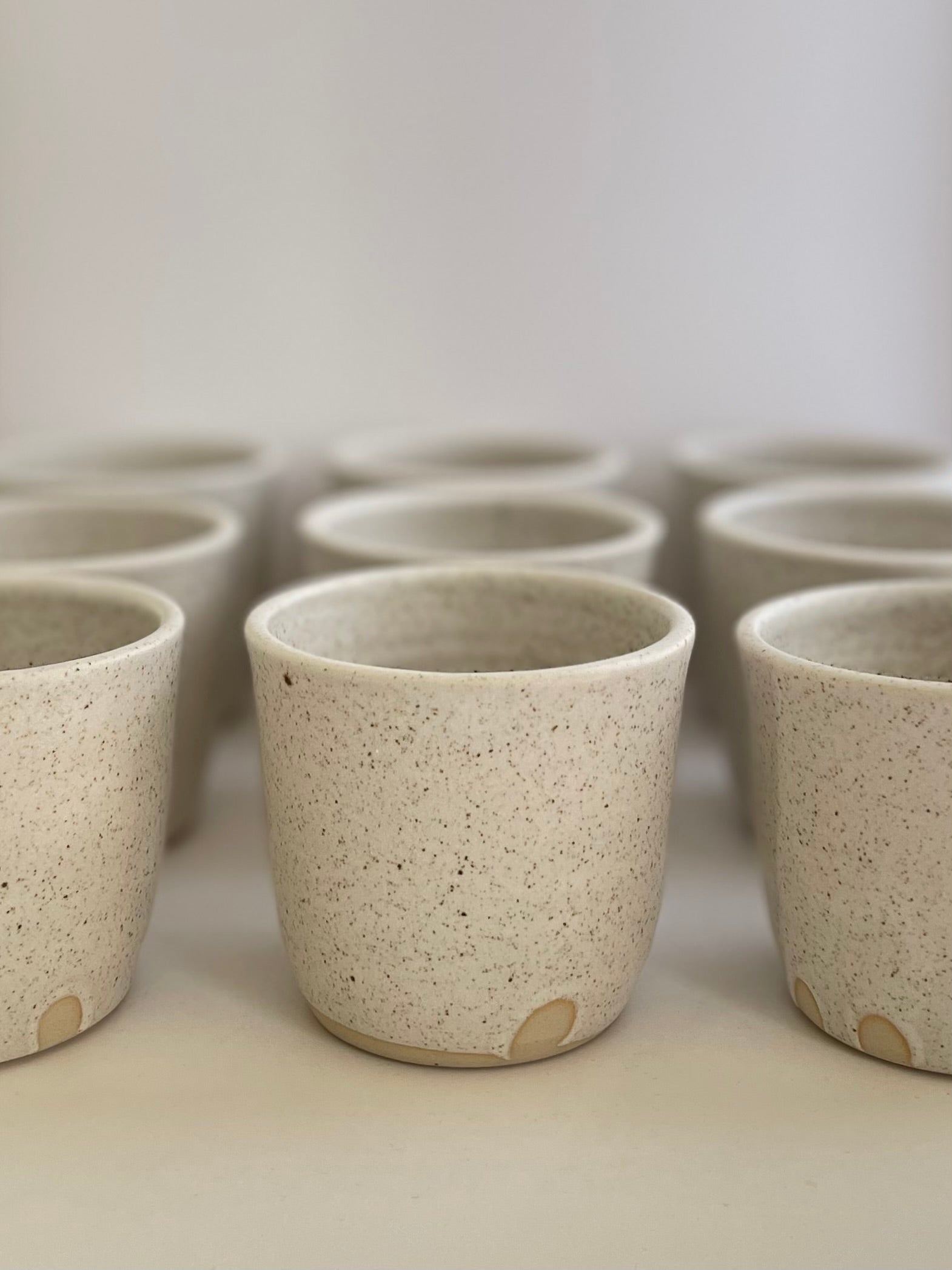 Collection of handmade ceramic coffee cups in a soft white speckled glaze.