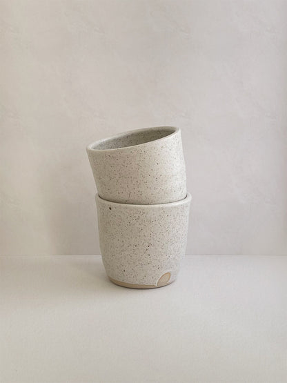 Two stacked white ceramic cups with a speckled texture on a neutral background.