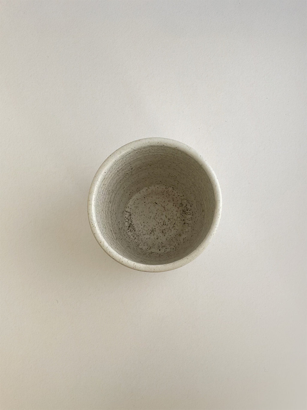 Speckled white ceramic cup on a neutral background - top view.