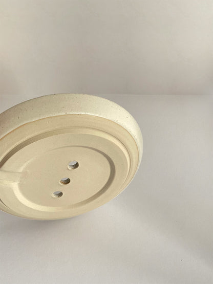 Close-up view of base of ceramic soap dish on a neutral background.