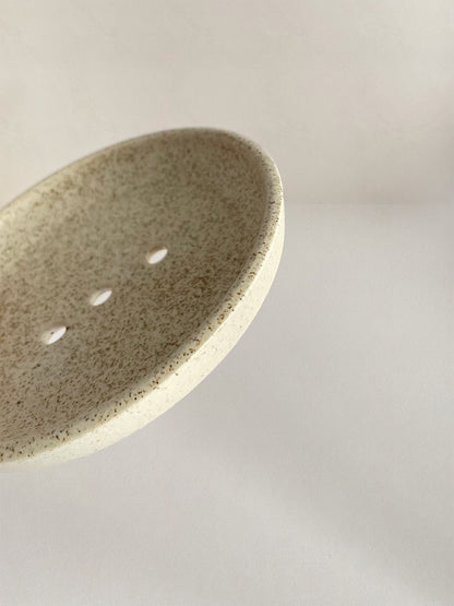 Close-up view of ceramic soap dish with speckled surface on a neutral background.