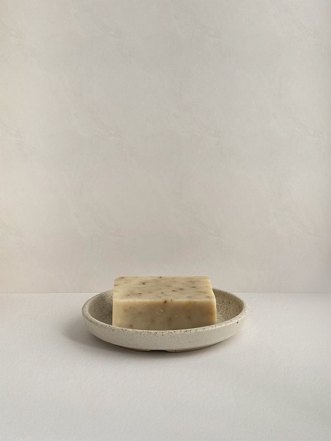Ceramic soap dish with bar of soap on a neutral background.