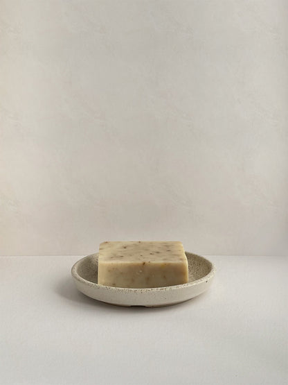 Ceramic soap dish with bar of soap on a neutral background.