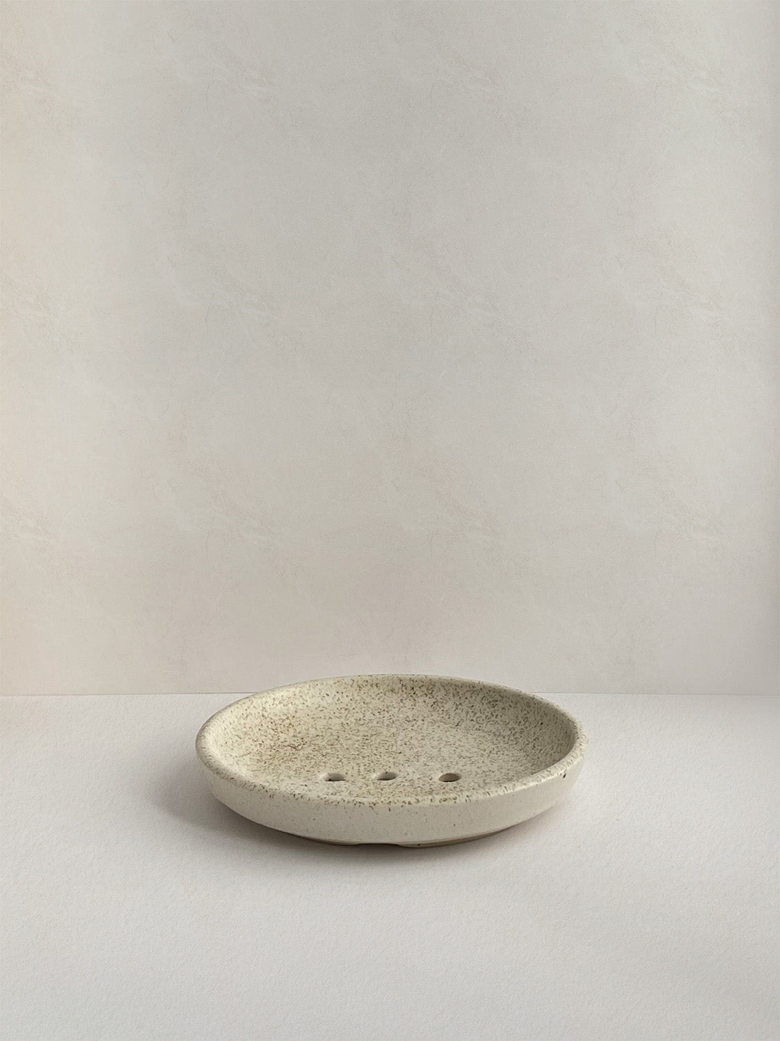 Ceramic soap dish with speckled surface on a neutral background - front view.