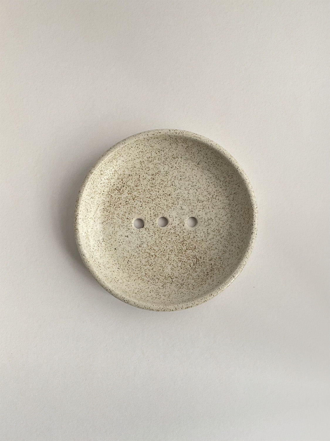 Ceramic soap dish with speckled surface on a neutral background - top view.