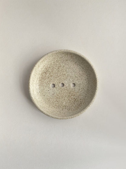 Ceramic soap dish with speckled surface on a neutral background - top view.