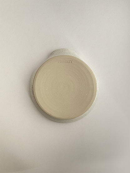 Speckled white ceramic spoon rest on a neutral background - base view.