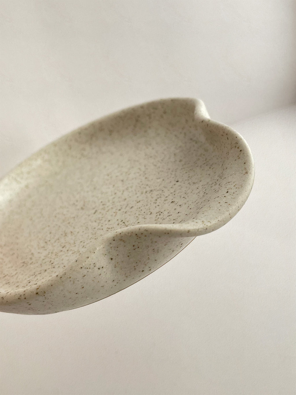 Close-up of speckled white handmade ceramic spoon rest on a neutral background.