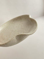 Close-up of speckled white handmade ceramic spoon rest on a neutral background.