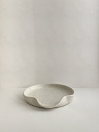 Speckled white handmade ceramic spoon rest on a neutral background - front view.