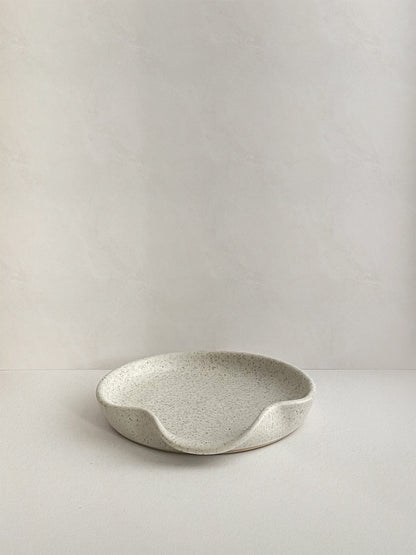Speckled white ceramic spoon rest on a neutral background - front view.