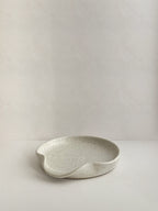 Speckled white handmade ceramic spoon rest on a neutral background - front view.