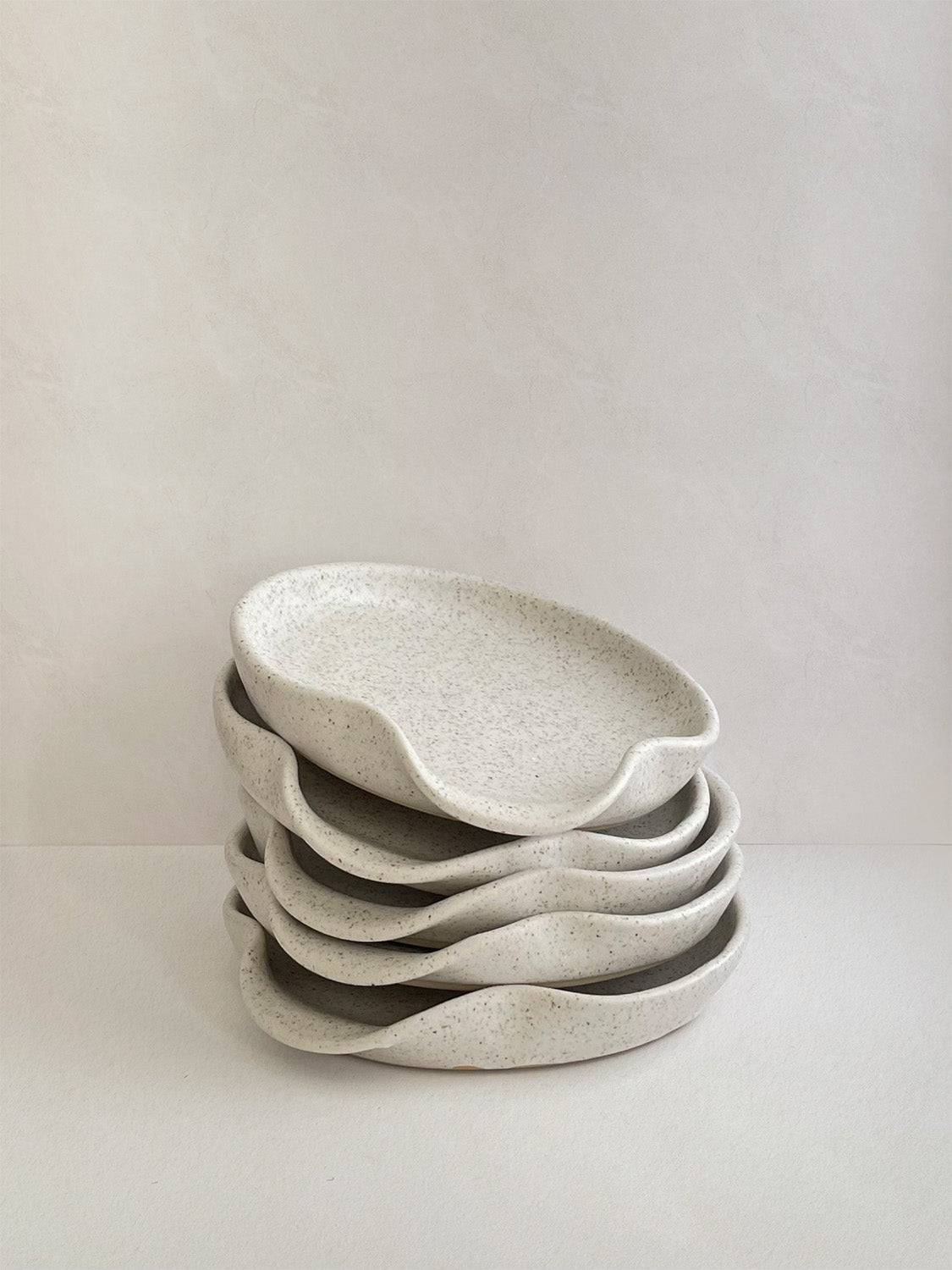 Stack of speckled white handmade ceramic spoon rests on a neutral background.