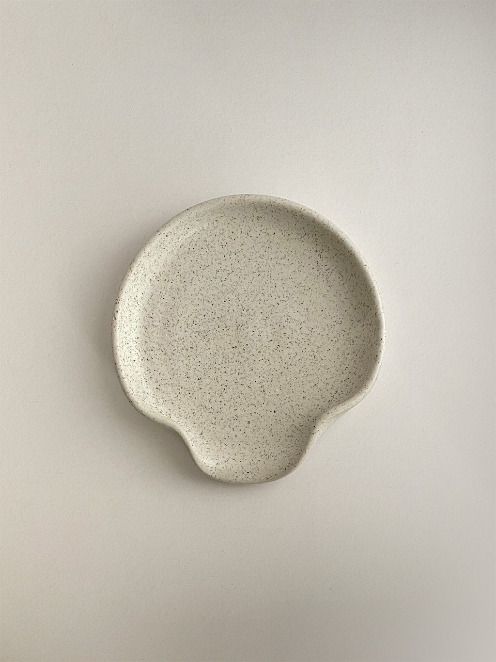 Speckled white handmade ceramic spoon rest on a neutral background - top view.