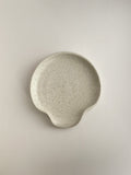 Speckled white handmade ceramic spoon rest on a neutral background - top view.