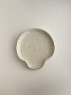 Speckled white handmade ceramic spoon rest on a neutral background - top view.