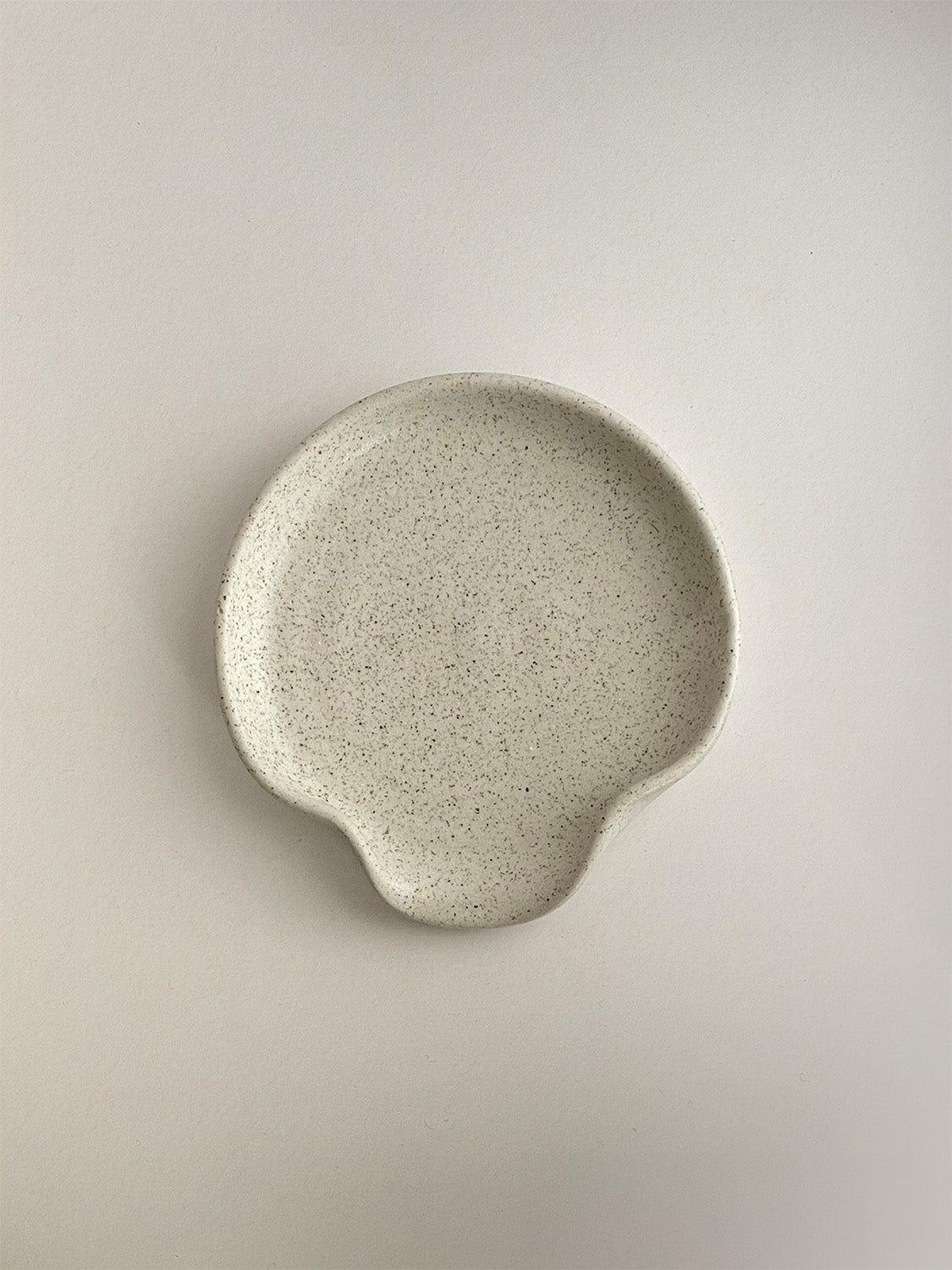 Speckled white handmade ceramic spoon rest on a neutral background - top view.