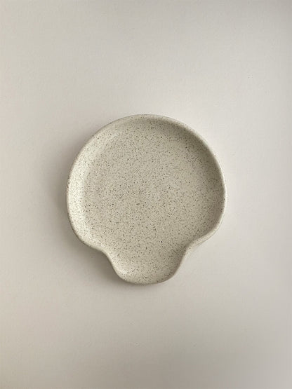 Speckled white ceramic spoon rest on a neutral background - top view.