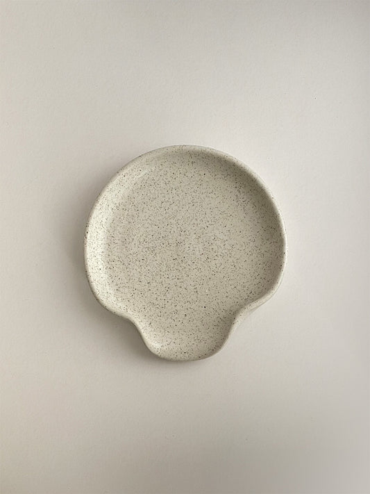 Speckled white ceramic spoon rest on a neutral background - top view.