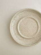 Speckled white ceramic candle holder on a neutral background - top detail.